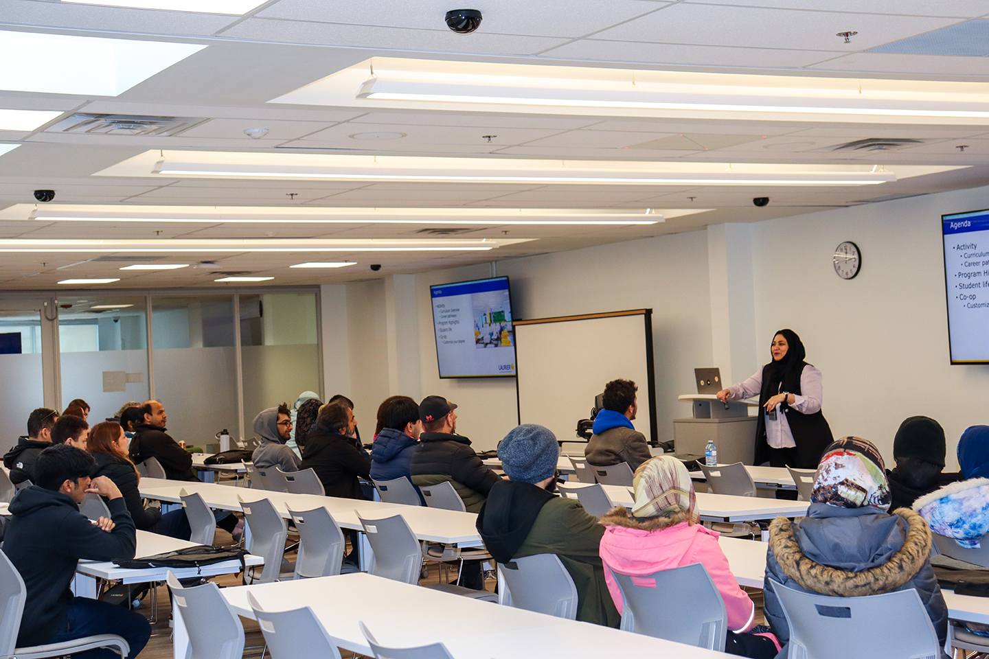 Audience sitting in rows of desks in a classroom listening to a presentation