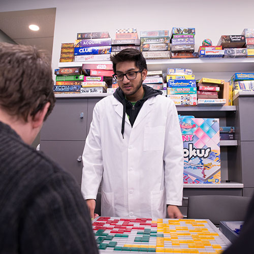Game design student presenting a game in front of a wall full of board game boxes
