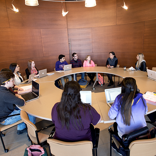 A small group of students sitting around a large circular table listening to a professor 