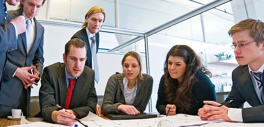Students in business attire leaned over a table reviewing charts