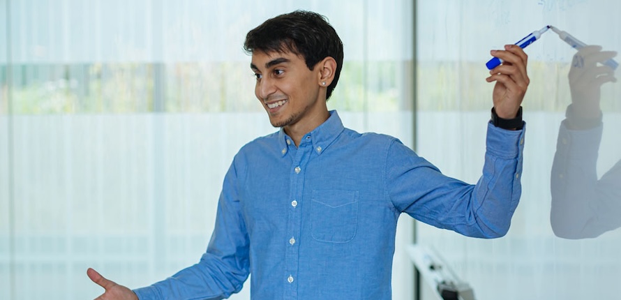 Student pointing to a whiteboard with a marker