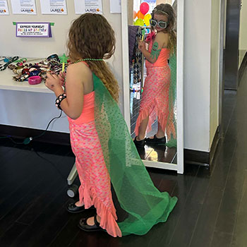 Young girl playing dress up in front of a mirror