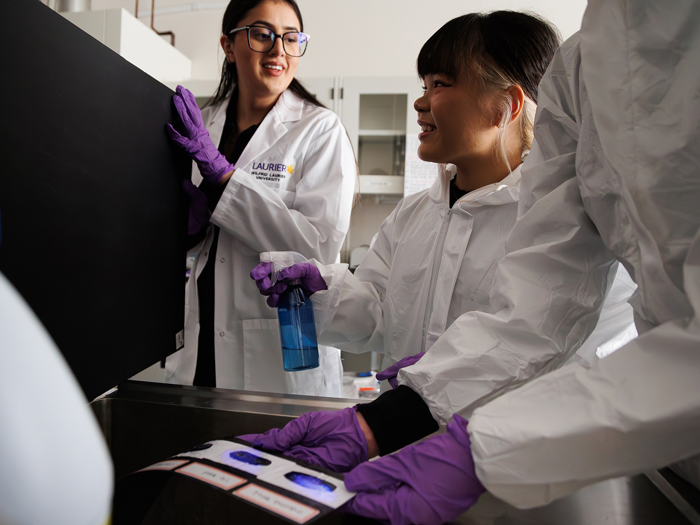 A student participant sprays evidence with luminol while a student researcher looks on