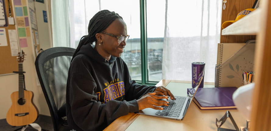 female student typing on her laptop in her residence room
