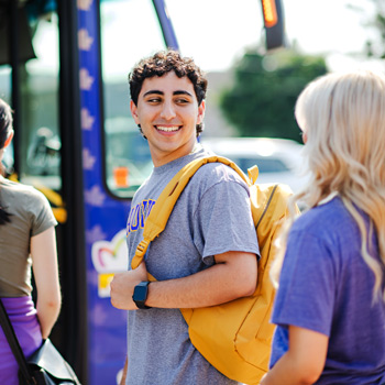 male student wearing yellow backpack smiling and waiting for bus