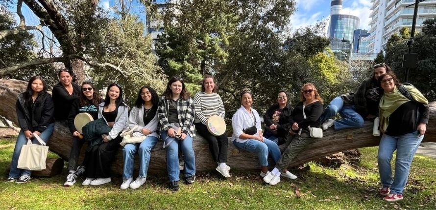 A group of women sitting on a log holding hand drums.