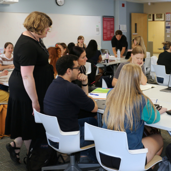 A woman overlooks a table of people having a discussion.