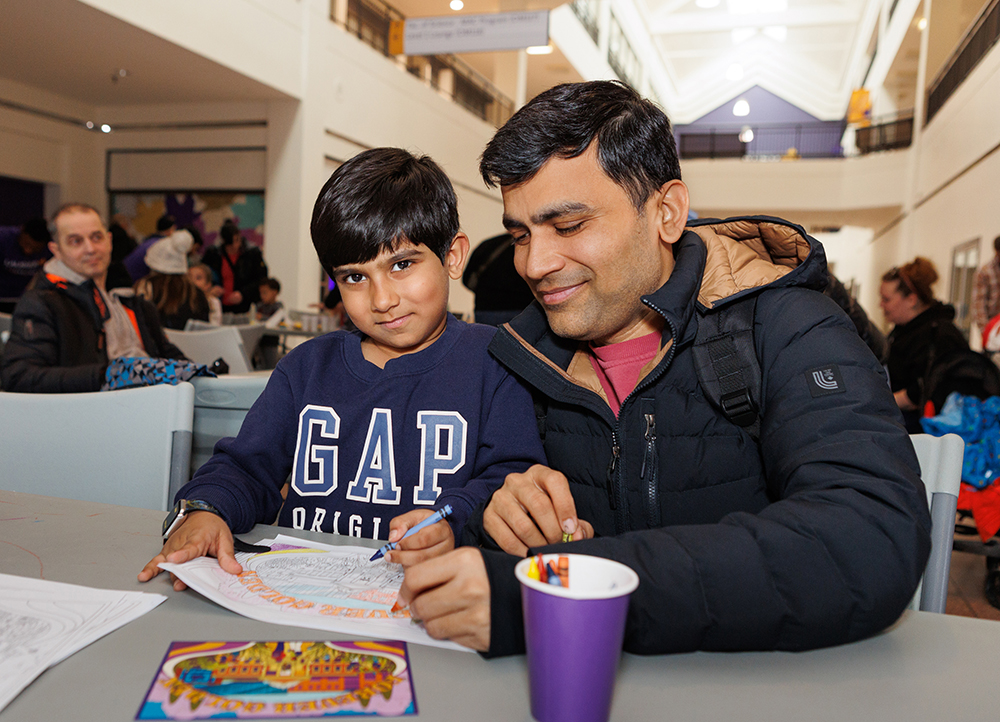 A child and father at the Purple and Gold Party colouring station.