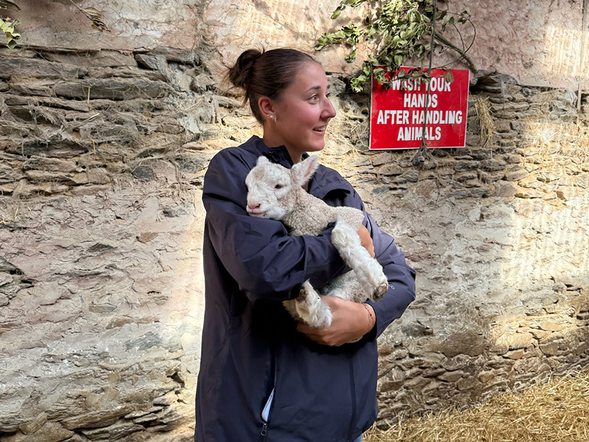 A young woman holds a baby lamb