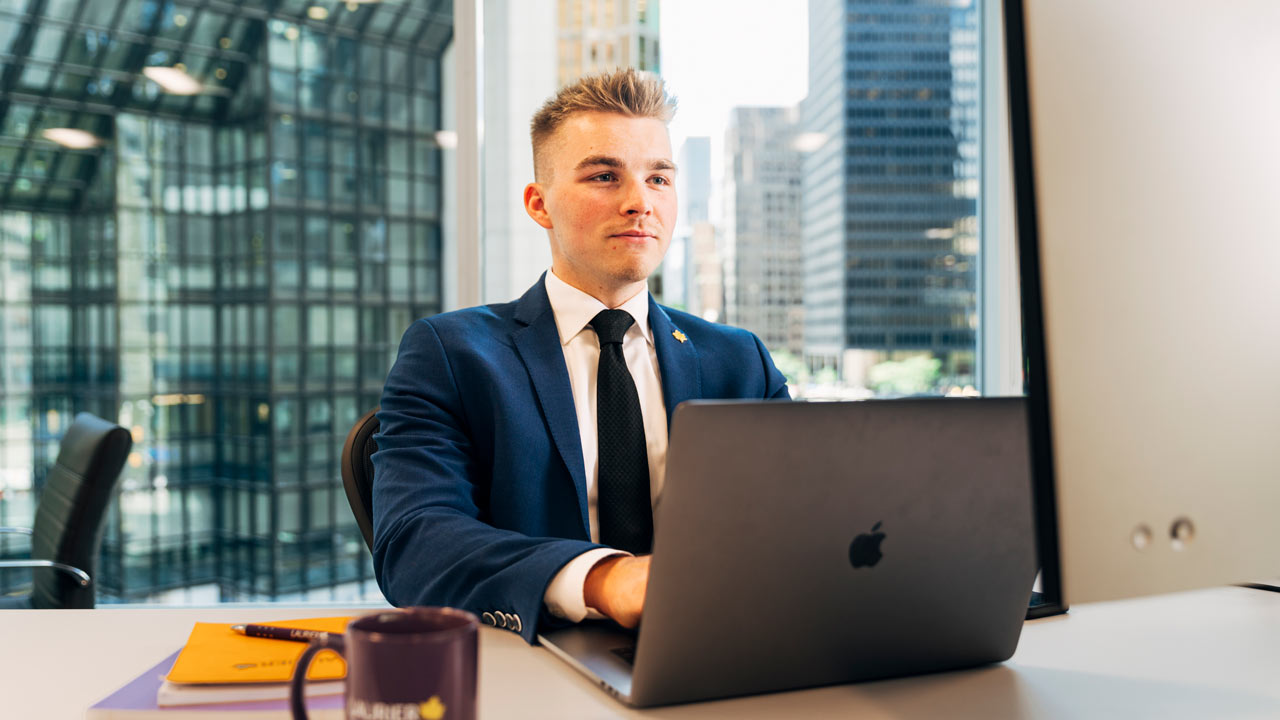 male student sitting at computer in a suit with city scape in the background