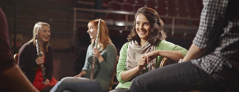 Student sitting in an auditorium holding instruments